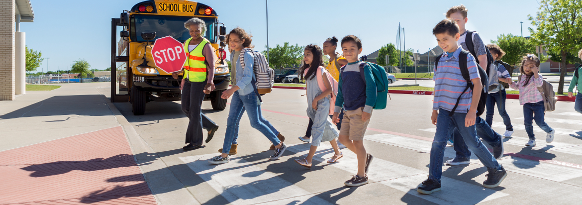 Healthy schools banner - students walking safely on pedestrian crossing, in front of school bus and crossing guard.