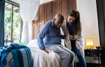 A senior man getting help from a healthcare worker to get out of bed