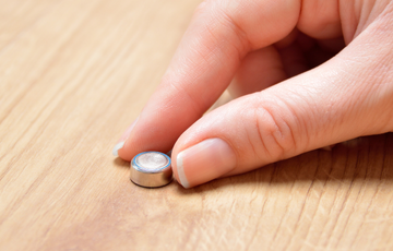 a button battery in between finger tips on a table